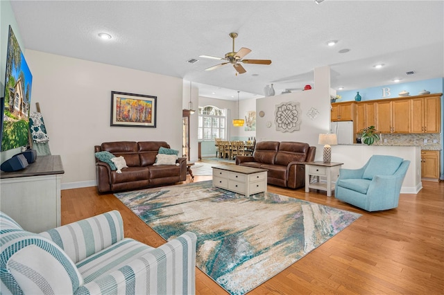 living area featuring light wood-style flooring, visible vents, a ceiling fan, and baseboards