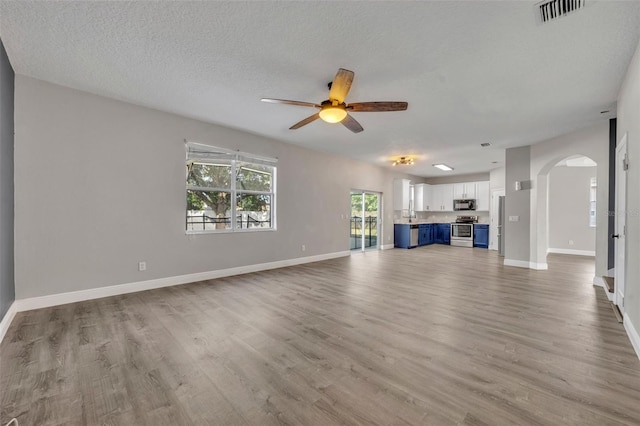 unfurnished living room featuring visible vents, arched walkways, ceiling fan, and light wood-style floors