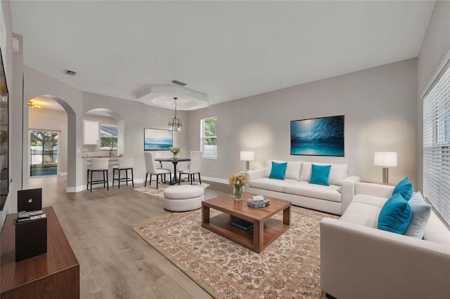 living room featuring arched walkways, visible vents, wood finished floors, and baseboards