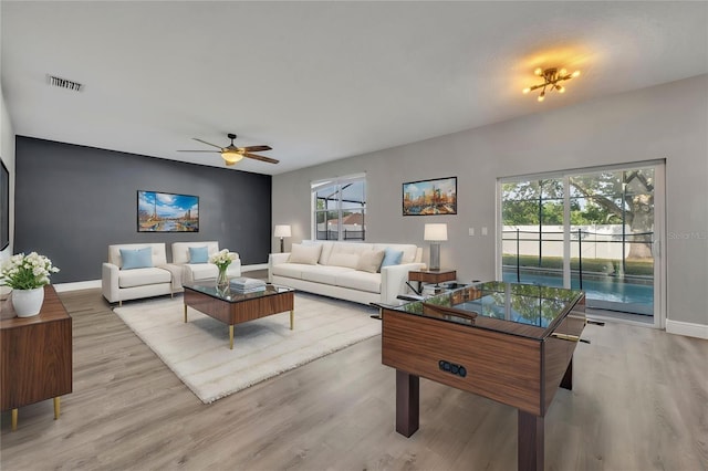 living room with light wood finished floors, a ceiling fan, visible vents, and baseboards