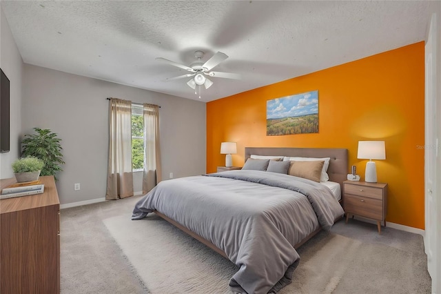bedroom featuring light colored carpet, a ceiling fan, a textured ceiling, and baseboards