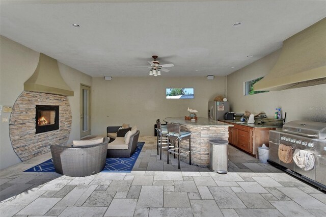 view of patio featuring a stone fireplace, an outdoor kitchen, and a ceiling fan