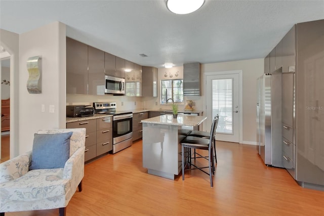 kitchen with appliances with stainless steel finishes, light wood-style flooring, a kitchen bar, gray cabinets, and a kitchen island