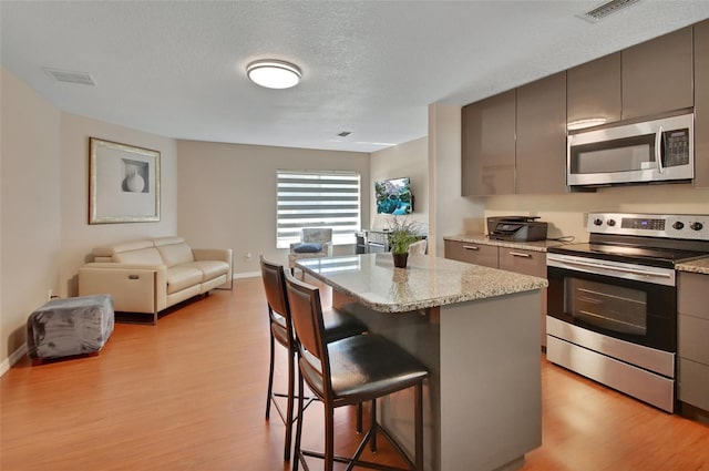 kitchen featuring stainless steel appliances, gray cabinets, a kitchen bar, a kitchen island, and light wood-style flooring