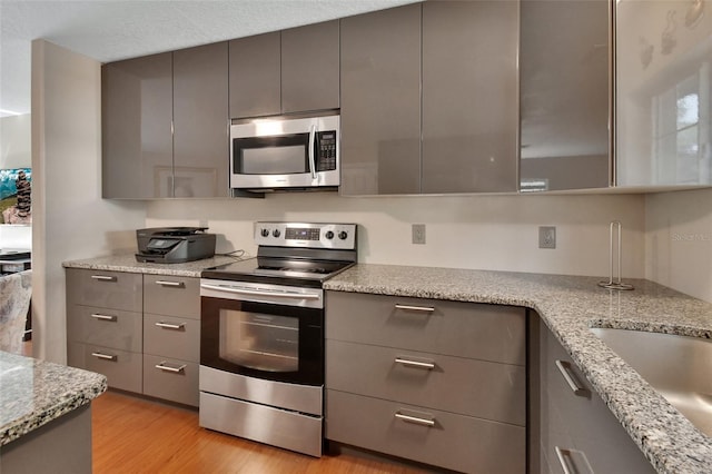 kitchen featuring stainless steel appliances, gray cabinets, light wood-style flooring, and light stone counters