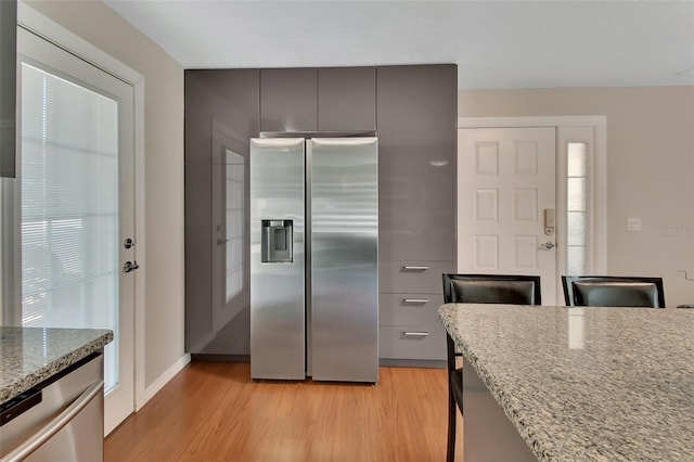 kitchen featuring appliances with stainless steel finishes, light wood finished floors, and light stone counters