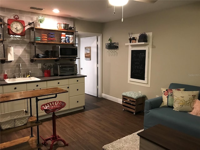 living area featuring baseboards, dark wood-type flooring, and a ceiling fan