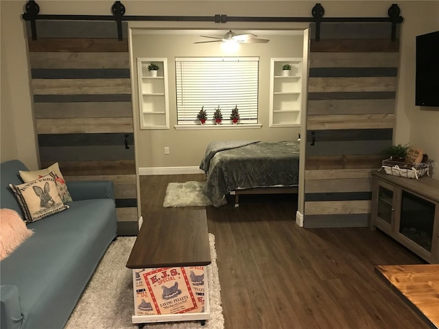 bedroom with a barn door, wood finished floors, wood walls, baseboards, and a ceiling fan