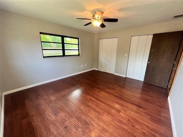 unfurnished bedroom featuring multiple closets, visible vents, baseboards, a textured ceiling, and wood finished floors