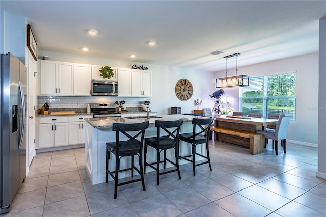 kitchen featuring visible vents, white cabinetry, backsplash, a breakfast bar, and appliances with stainless steel finishes
