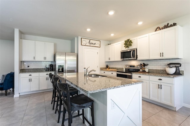 kitchen with a kitchen island with sink, a sink, decorative backsplash, a breakfast bar, and appliances with stainless steel finishes