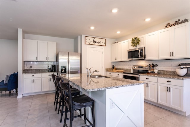 kitchen featuring a sink, a center island with sink, tasteful backsplash, a breakfast bar, and appliances with stainless steel finishes