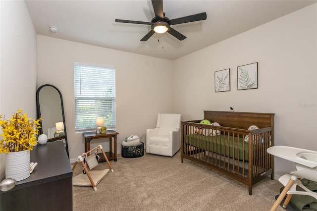 carpeted bedroom with ceiling fan and a nursery area