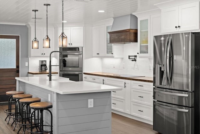 kitchen with wood finished floors, white cabinets, backsplash, appliances with stainless steel finishes, and custom range hood