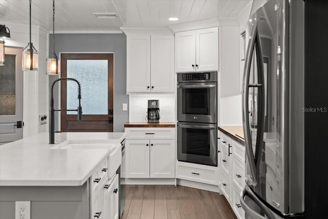 kitchen featuring hanging light fixtures, visible vents, white cabinetry, crown molding, and appliances with stainless steel finishes