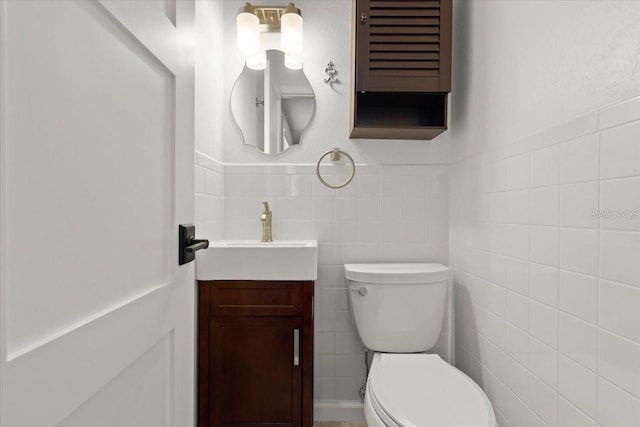 bathroom featuring tile walls, toilet, vanity, and a wainscoted wall