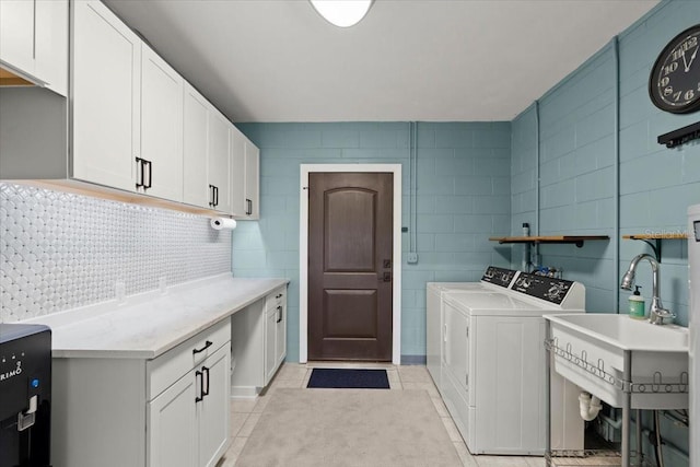 laundry area with tile walls, light tile patterned floors, washer and dryer, a sink, and cabinet space