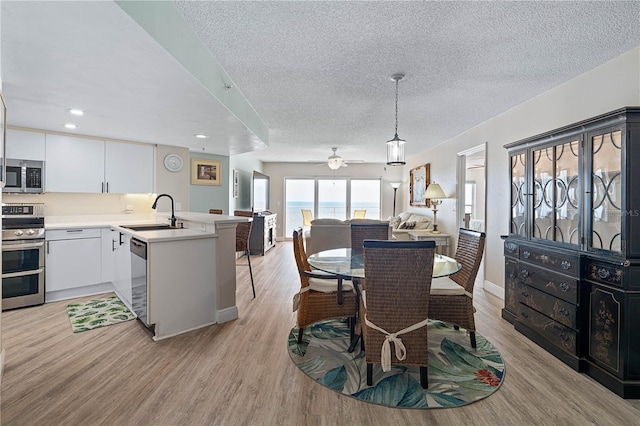 dining space with baseboards, a textured ceiling, ceiling fan, and light wood-style flooring