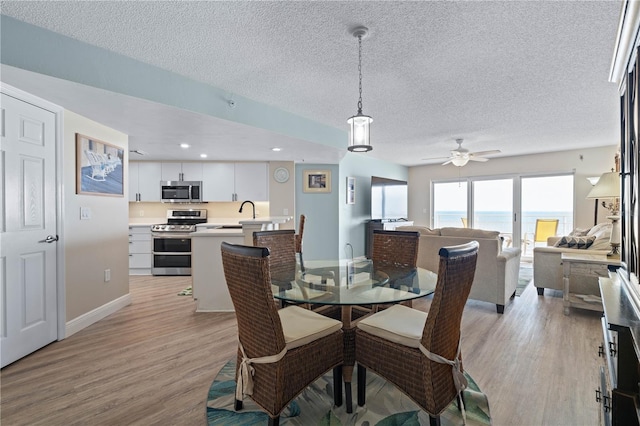 dining area featuring a ceiling fan, baseboards, light wood finished floors, and a textured ceiling