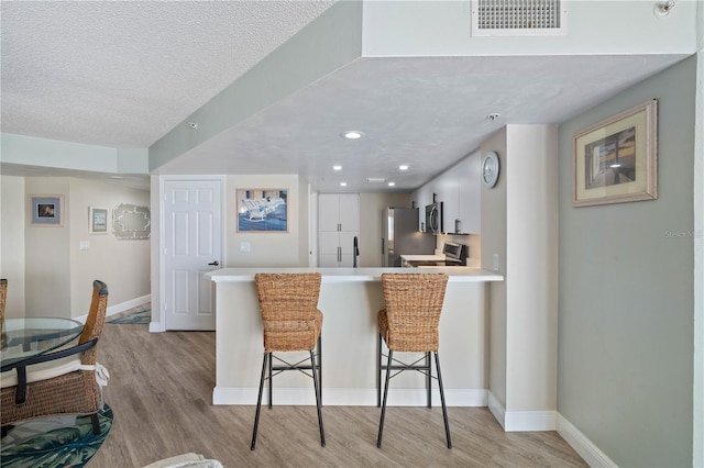 kitchen featuring appliances with stainless steel finishes, light wood-style floors, light countertops, a kitchen breakfast bar, and a peninsula