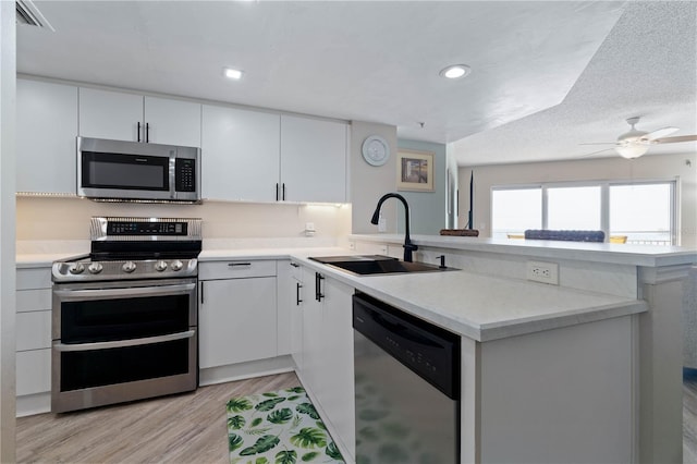 kitchen featuring appliances with stainless steel finishes, light wood-type flooring, a sink, light countertops, and a peninsula