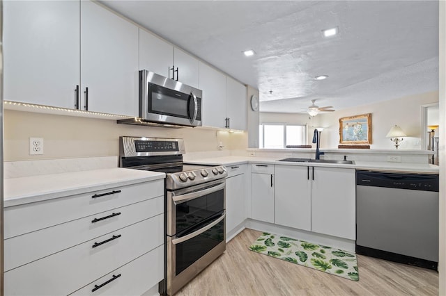 kitchen featuring appliances with stainless steel finishes, a sink, light countertops, a ceiling fan, and light wood-type flooring