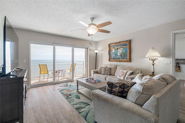 living room featuring a ceiling fan, a textured ceiling, a water view, and wood finished floors