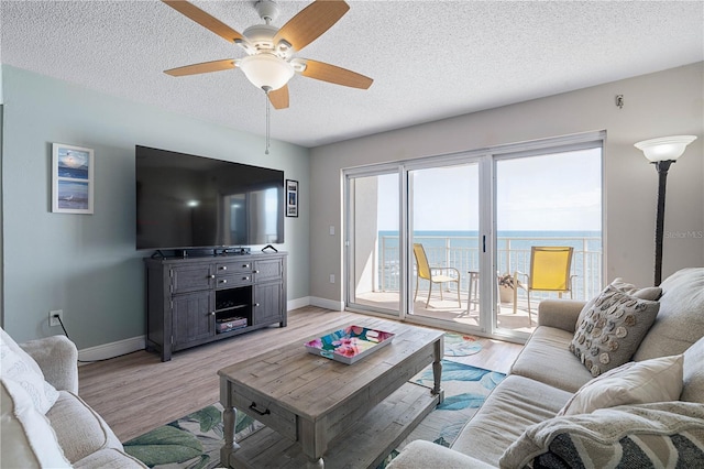 living area with a textured ceiling, ceiling fan, baseboards, and light wood-style flooring