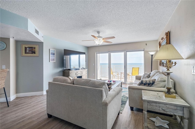 living area featuring a textured ceiling, a ceiling fan, baseboards, wood finished floors, and visible vents