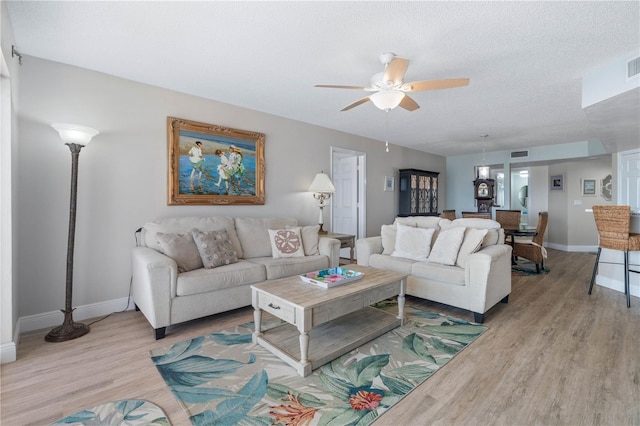 living room featuring baseboards, ceiling fan, light wood-style flooring, and visible vents