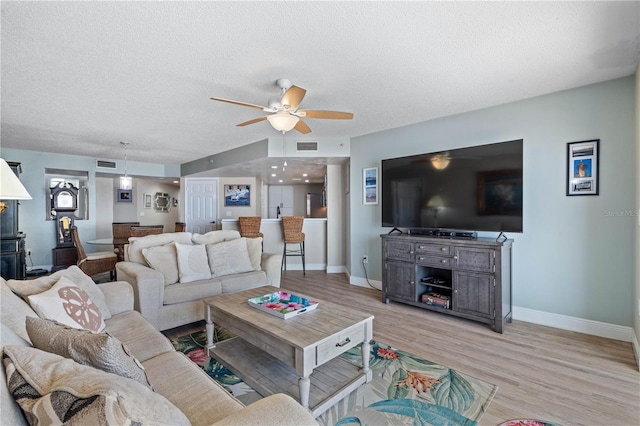 living room with light wood-style floors, a ceiling fan, baseboards, and a textured ceiling