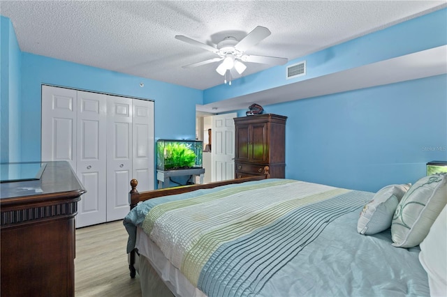 bedroom featuring a ceiling fan, a textured ceiling, visible vents, a closet, and light wood-style flooring