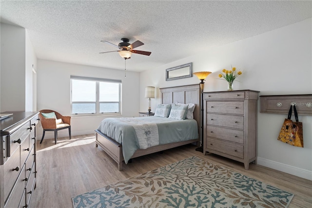 bedroom with baseboards, a textured ceiling, light wood finished floors, and ceiling fan