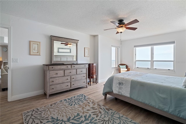 bedroom featuring baseboards, ceiling fan, light wood-style flooring, and a textured ceiling