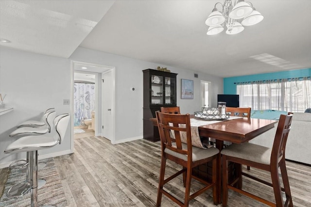 dining area featuring light wood finished floors, a notable chandelier, and baseboards