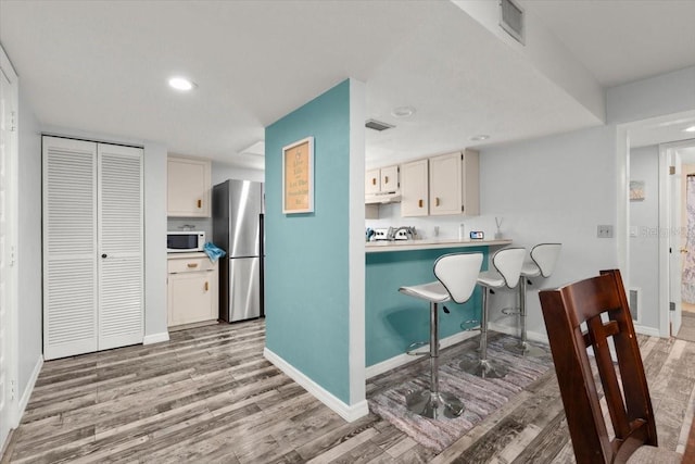 kitchen with light wood-style flooring, white microwave, freestanding refrigerator, and baseboards