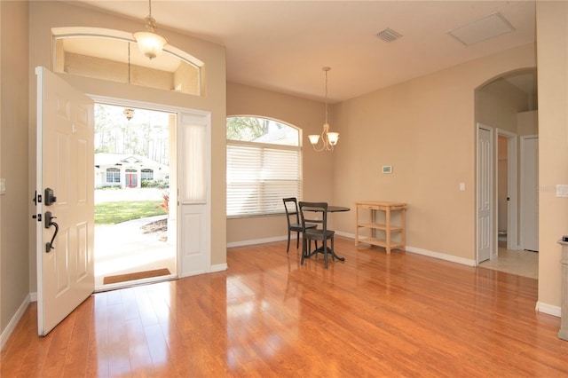 foyer entrance featuring visible vents, baseboards, an inviting chandelier, arched walkways, and light wood finished floors