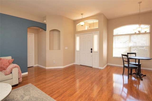 foyer entrance featuring baseboards, wood finished floors, a notable chandelier, and arched walkways
