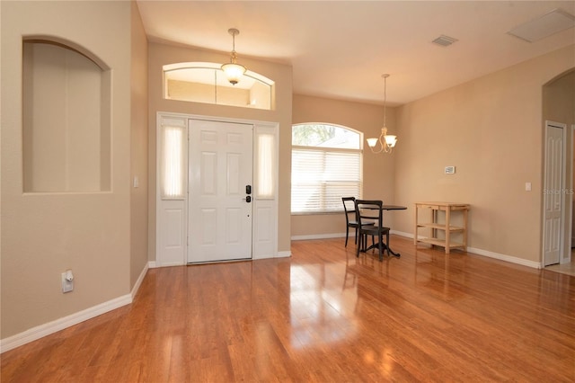 foyer entrance featuring visible vents, a chandelier, arched walkways, baseboards, and wood finished floors