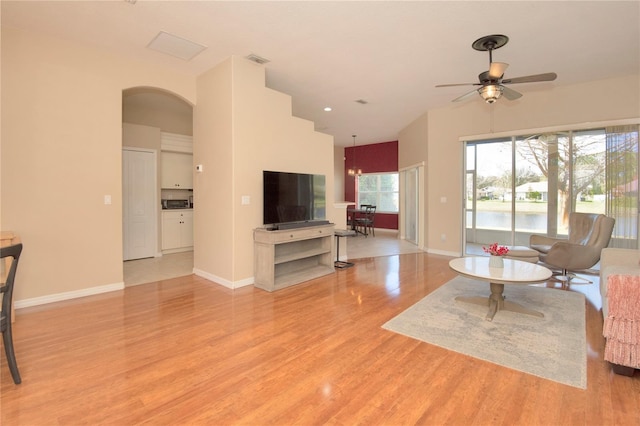 living room with light wood-style flooring, visible vents, arched walkways, baseboards, and a ceiling fan