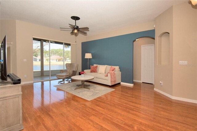 living room featuring baseboards, wood finished floors, a ceiling fan, and arched walkways