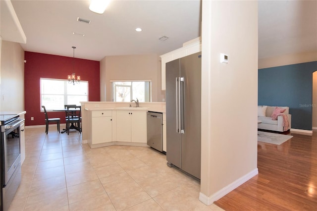 kitchen featuring appliances with stainless steel finishes, an inviting chandelier, a peninsula, and a healthy amount of sunlight