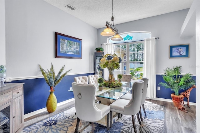 dining area with baseboards, visible vents, a textured ceiling, and wood finished floors