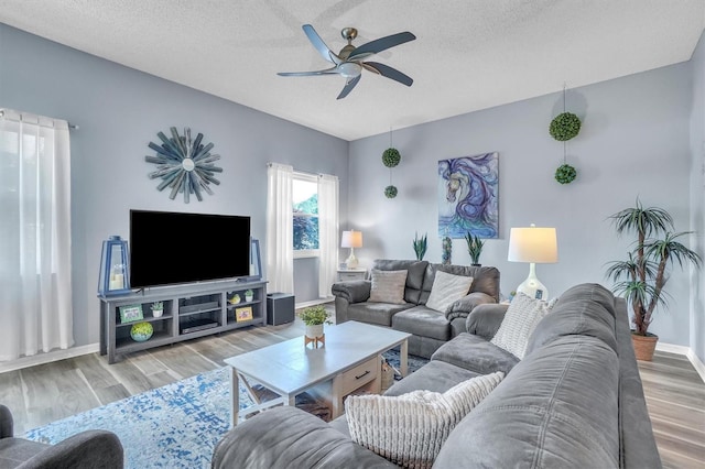 living area featuring a textured ceiling, baseboards, a ceiling fan, and wood finished floors