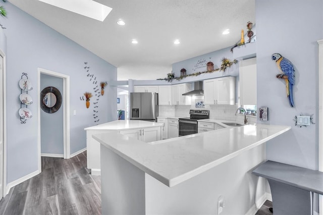 kitchen featuring a sink, wood finished floors, backsplash, wall chimney range hood, and appliances with stainless steel finishes