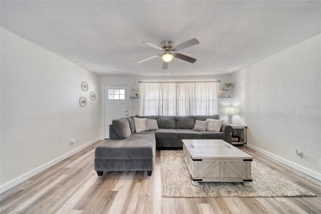 living room with a textured ceiling, a textured wall, baseboards, wood finished floors, and a ceiling fan