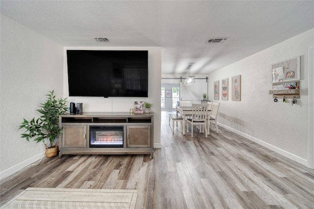 living area with visible vents, light wood-style floors, and a textured wall