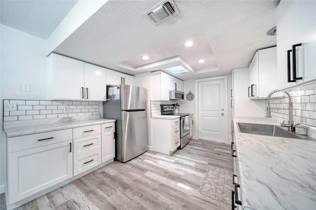 kitchen with a textured ceiling, a sink, appliances with stainless steel finishes, visible vents, and light wood finished floors