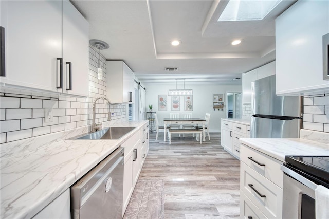 kitchen with recessed lighting, a sink, stainless steel appliances, a tray ceiling, and white cabinets