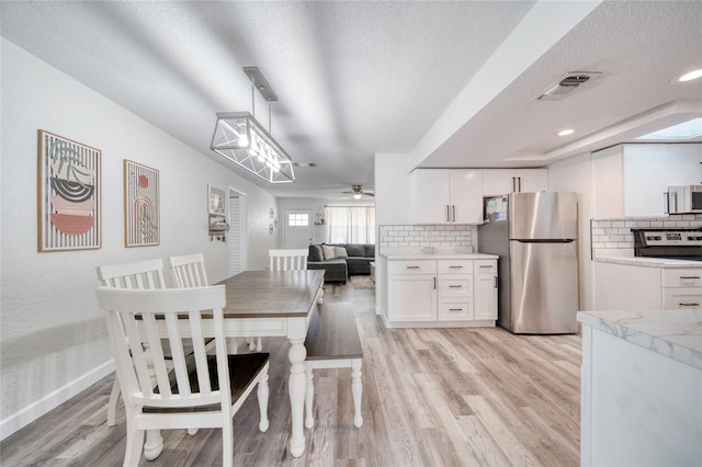 dining area with a textured ceiling, visible vents, baseboards, light wood-type flooring, and a ceiling fan